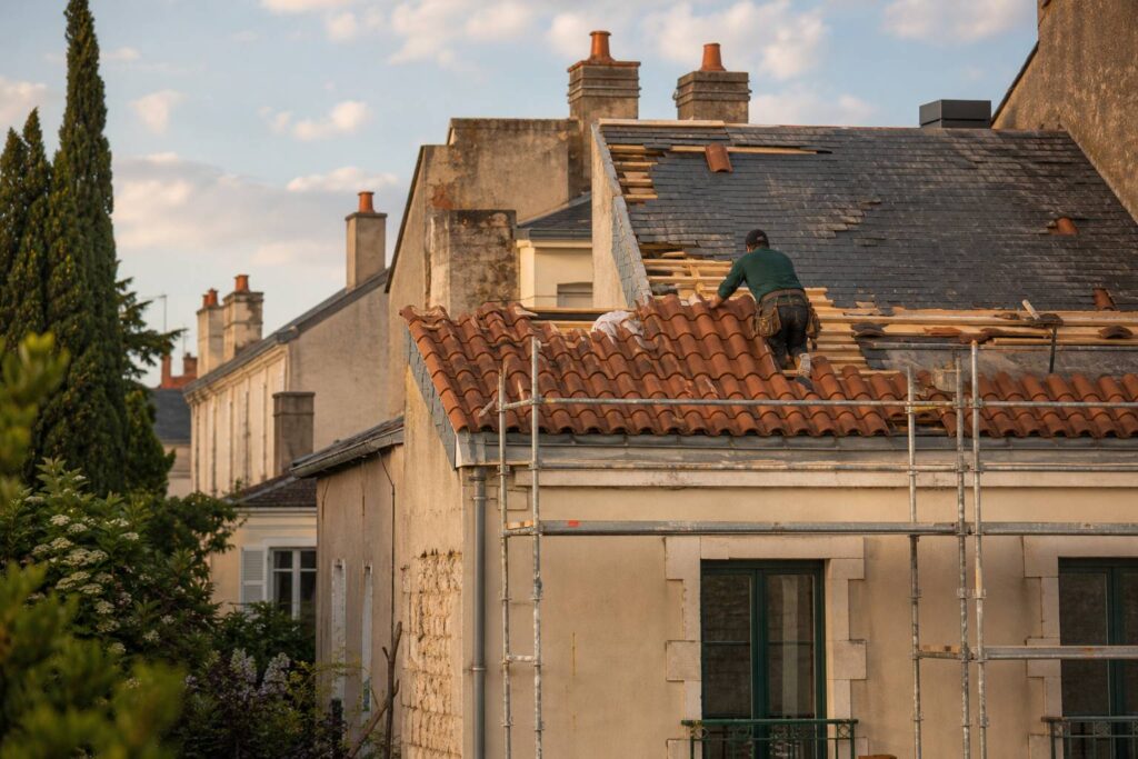 Artisan couvreur posant des tuiles sur une toiture en cours de rénovation à Nantes en fin d'après-midi