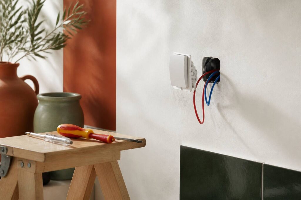 Interrupteur démonté avec fils électriques apparents sur un mur clair